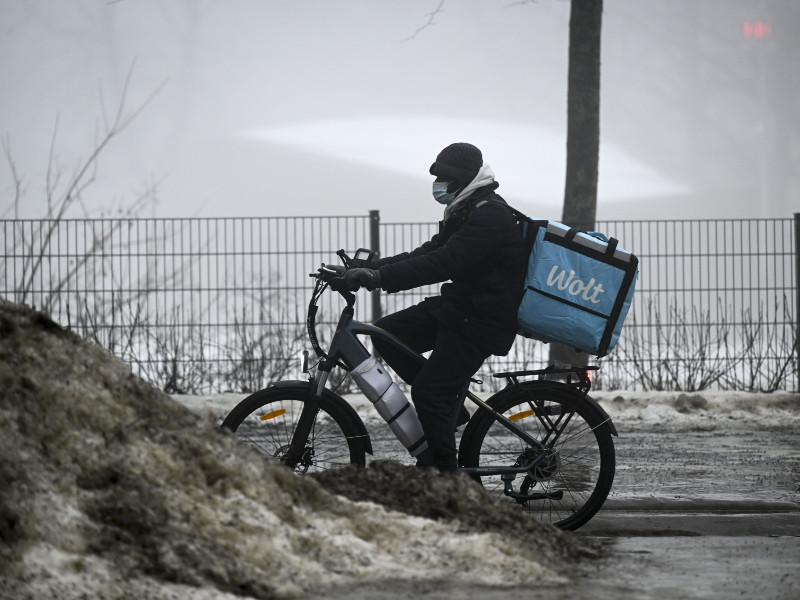A Wolt courier riding a bicycle by a pile of dirty snow in foggy Helsinki on 31 January 2024.